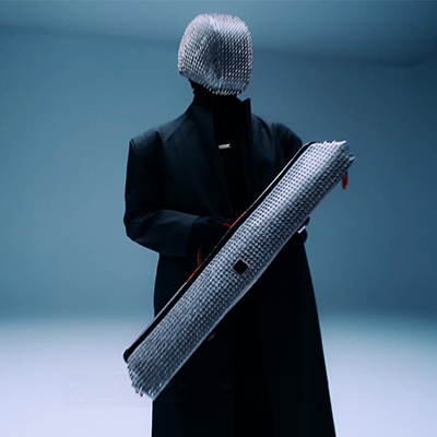 Black figure, silver mask, holds perforated case.